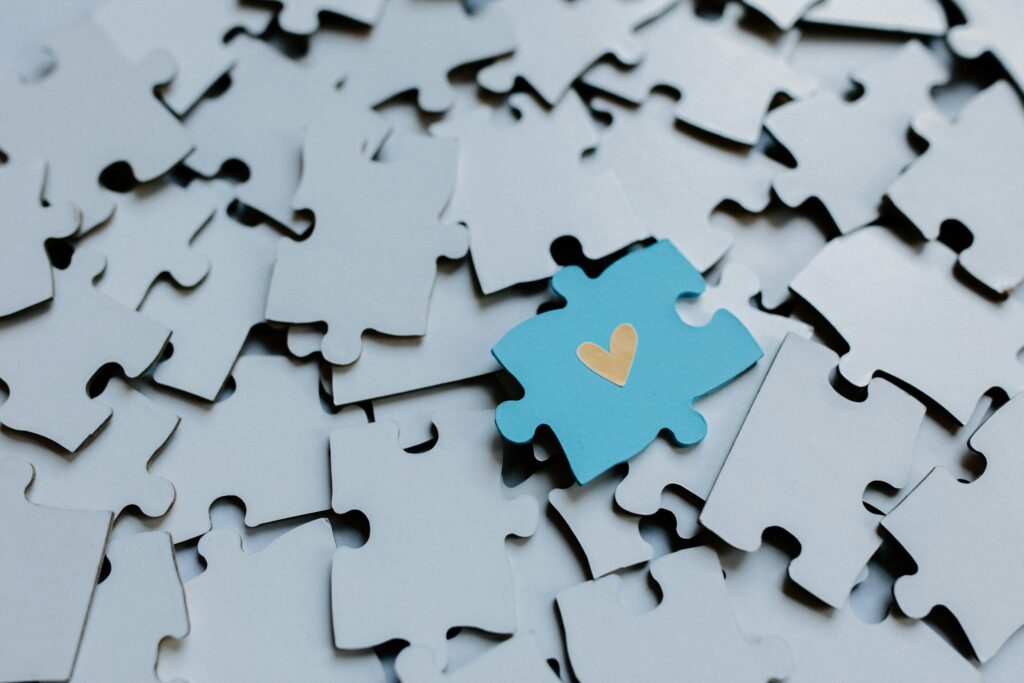 Puzzelstukjes op elkaar in het grijs. één puzzelstukje is blauw met een geel hartje erop.