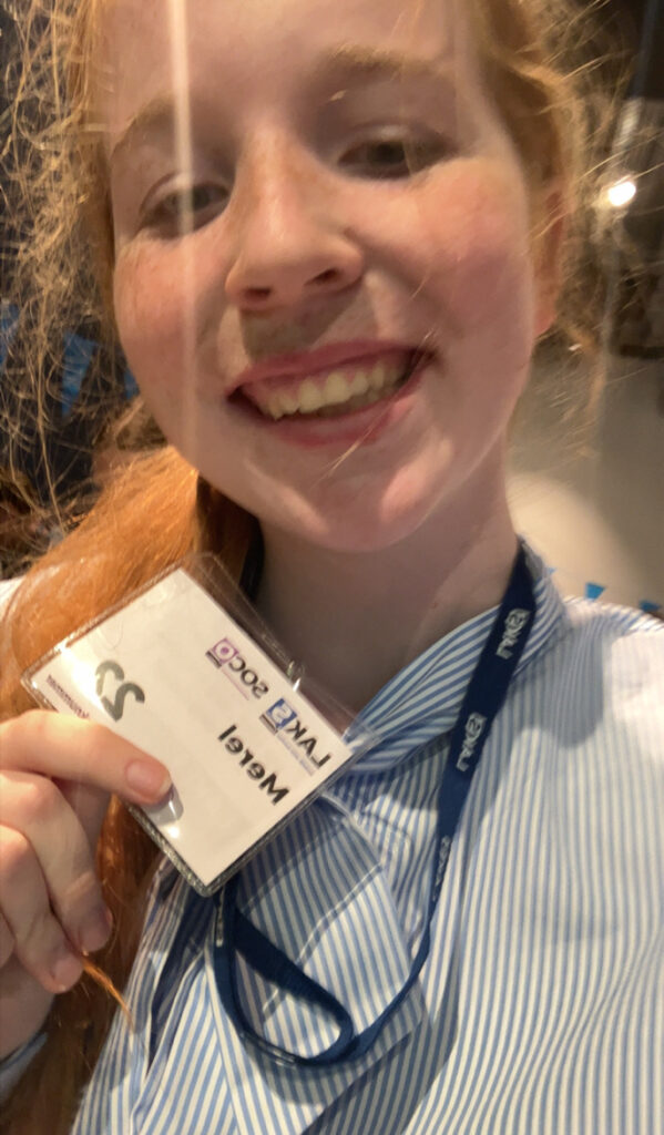 een foto van mij waar ik een kaartje vasthoud. Hierop staat: LAKS SoCo en mijn naam Merel. Ook staat er mijn sprekers nummer op namelijk nummer 22!